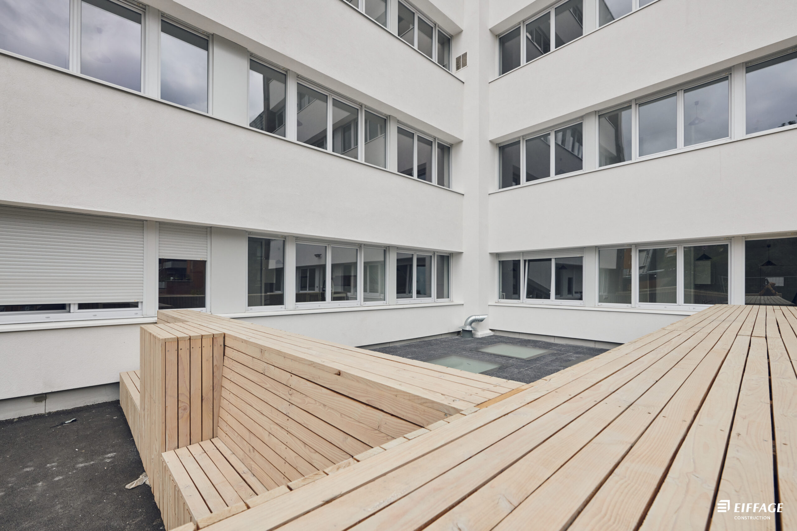 Cour de la résidence Vivaldi à Villeneuve-d’Ascq après réhabilitation, avec terrasse en bois, août 2024
