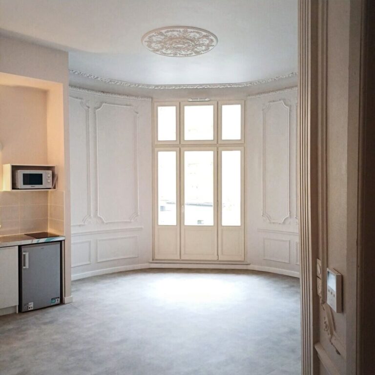 Pièce lumineuse aux murs moulurés avec portes-fenêtres et kitchenette dans un intérieur rénové